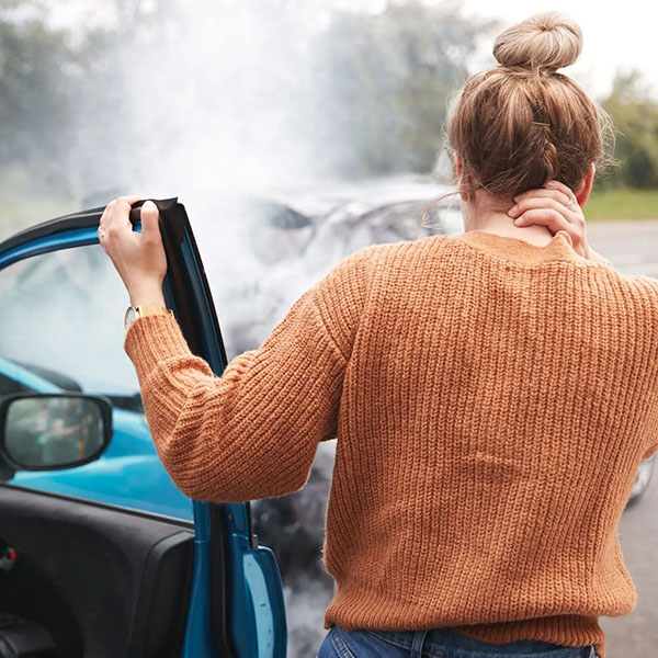auto-accidents2 woman standing next to her car after an auto accident with one hand holding the open car door and the other holding the back of her neck